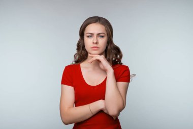 Hmm, ilginç. Düşünceli genç esmer kadın, kameraya bakıyor ve bir şeyler düşünüyor, varsayımda bulunuyor, düşünüyor. Stüdyo fotoğrafı, gri arka plan. İnsani duygular, yüz ifadesi kavramı