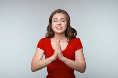 Lütfen. Sevimli genç esmer kadın dilenci tabelasında el ele tutuşuyor, yardım istiyor, yardıma ihtiyacı var, gülümsüyor sevimli, gri arka planda duruyor.