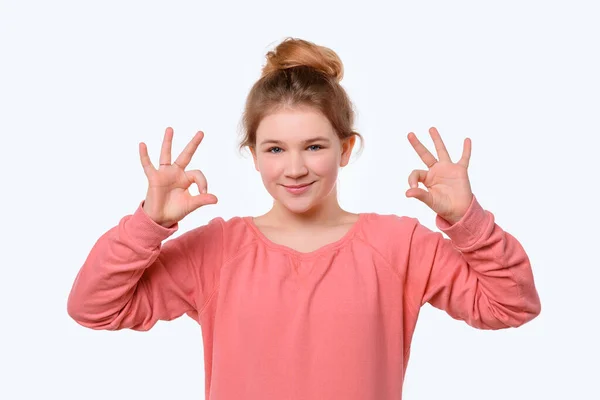 両手でOkのジェスチャーを見せるピンクのカジュアルなスウェットシャツ姿の可愛い少女のポートレート 白地だ 人間の感情やジェスチャーの概念 — ストック写真