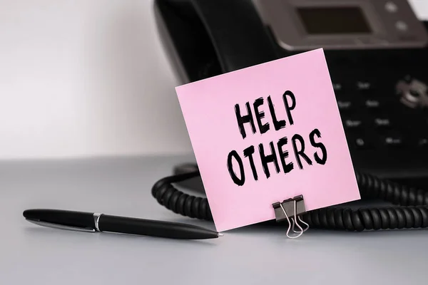 The text Help Others written on a pink sticky note to remind you an important event. Closeup of a personal agenda. Conceptual photo