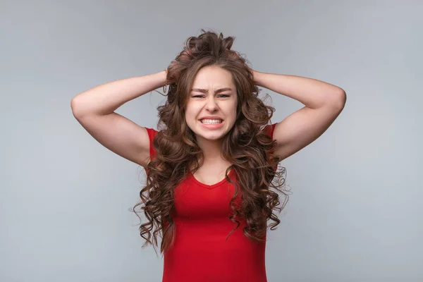 Kız olumsuz duyguları içinde tutamaz. Depresyonda olan, kırmızı tişörtlü, elleri saçında, yüzünü buruşturan, ruhunda acı hisseden, kızgın bir esmer kadın.