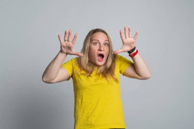 Sarı tişörtlü endişeli kadın ellerini açtı. Gerçek insani tepkiler, duygular ve duygular. Stüdyo çekimi, gri arkaplan