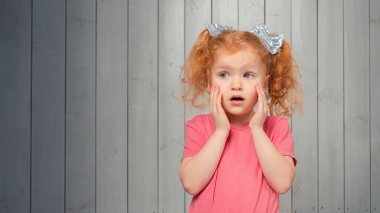 Şok olmuş ve korkmuş, 4-6 yaşlarında küçük bir kız, sola bakıyor ve korkmuş, korkunç bir şeyden korkuyor. Stüdyo çekimi, hafif ahşap arka plan. Boşluğu kopyala