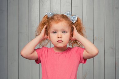Endişeli ve sorunlu kızıl saçlı 4-6 yaşlarında küçük bir kız başının üstünde duruyor ve kaşlarını çatıyor, sorunları var, unutma. Stüdyo çekimi, hafif ahşap arka plan