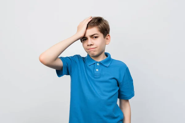 Shocked Serious boy 12-14 years old in casual blue t shirt, look puzzled and amazed, holding hand on head, staring at problem, forgot remember something, standing against light gray background, isolated