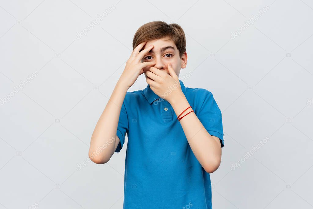 Anxious and scared teen boy looking frightened, staring at camera with nervous face, fear of consequences, standing alarmed against light gray background