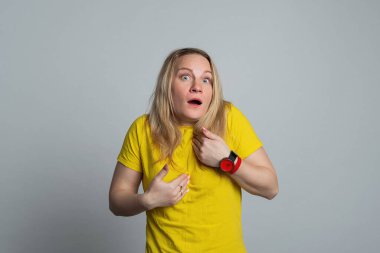 Kafası karışmış bir kadın şüpheli ve üzgün bir yüzle kendini işaret ediyor. Benim jestimden mi bahsediyorsun, sana bakmamdan mı? Stüdyo çekimi, gri arka plan, jest konsepti