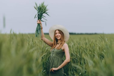 Şapkalı genç bir kadın buğday tarlasında yürüyor, hayattan ve yazdan zevk alıyor. Buğday tarlası. Güneş ışığı altında güzel doğa manzarası. Sağlıklı yaşam tarzı kavramı. Gürültülü görüntü, film tahılı