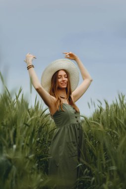Şapkalı genç bir kadın buğday tarlasında yürüyor, hayattan ve yazdan zevk alıyor. Buğday tarlası. Güneş ışığı altında güzel doğa manzarası. Sağlıklı yaşam tarzı kavramı. Gürültülü görüntü, film tahılı