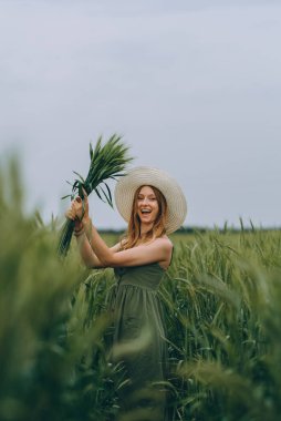 Şapkalı genç bir kadın buğday tarlasında yürüyor, hayattan ve yazdan zevk alıyor. Buğday tarlası. Güneş ışığı altında güzel doğa manzarası. Sağlıklı yaşam tarzı kavramı. Gürültülü görüntü, film tahılı