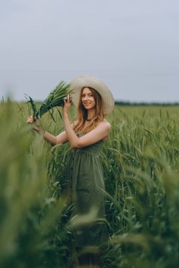 Şapkalı genç bir kadın buğday tarlasında yürüyor, hayattan ve yazdan zevk alıyor. Buğday tarlası. Güneş ışığı altında güzel doğa manzarası. Sağlıklı yaşam tarzı kavramı. Gürültülü görüntü, film tahılı