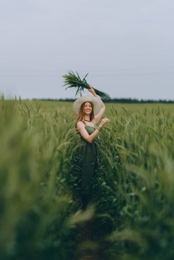 Şapkalı genç bir kadın buğday tarlasında yürüyor, hayattan ve yazdan zevk alıyor. Buğday tarlası. Güneş ışığı altında güzel doğa manzarası. Sağlıklı yaşam tarzı kavramı. Gürültülü görüntü, film tahılı