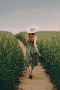 Şapkalı genç bir kadın buğday tarlasında yürüyor, hayattan ve yazdan zevk alıyor. Buğday tarlası. Güneş ışığı altında güzel doğa manzarası. Sağlıklı yaşam tarzı kavramı. Gürültülü görüntü, film tahılı