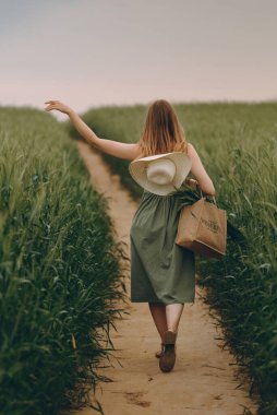 Genç bir kadın buğday tarlasında yürüyor, hayatın ve yazın tadını çıkarıyor. Buğday tarlası. Güneş ışığı altında güzel doğa manzarası. Sağlıklı yaşam tarzı kavramı. Gürültülü görüntü, film tahılı