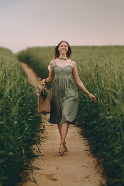 Genç bir kadın buğday tarlasında yürüyor, hayatın ve yazın tadını çıkarıyor. Buğday tarlası. Güneş ışığı altında güzel doğa manzarası. Sağlıklı yaşam tarzı kavramı. Gürültülü görüntü, film tahılı