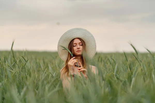 Young woman in a wheat field on a sunset background. Wheat field. Beautiful Nature Sunset Landscape. Model in a hat in the field. Rich harvest Concept. Image with noise, film grain