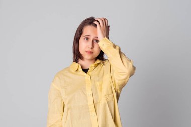 Kafası karışmış genç bir kızın portresi sarı bir gömlek giymiş, gri arka planda duran, izole edilmiş bir şeyi hatırlamaya çalışıyor.