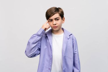 Ciddi bir çocuk, 12-14 yaşlarında, açık gri arka planda şık bir gömlek giyip bir fikir üretiyor. Düşünce anlayışı. Akıllı ol ve düşün.