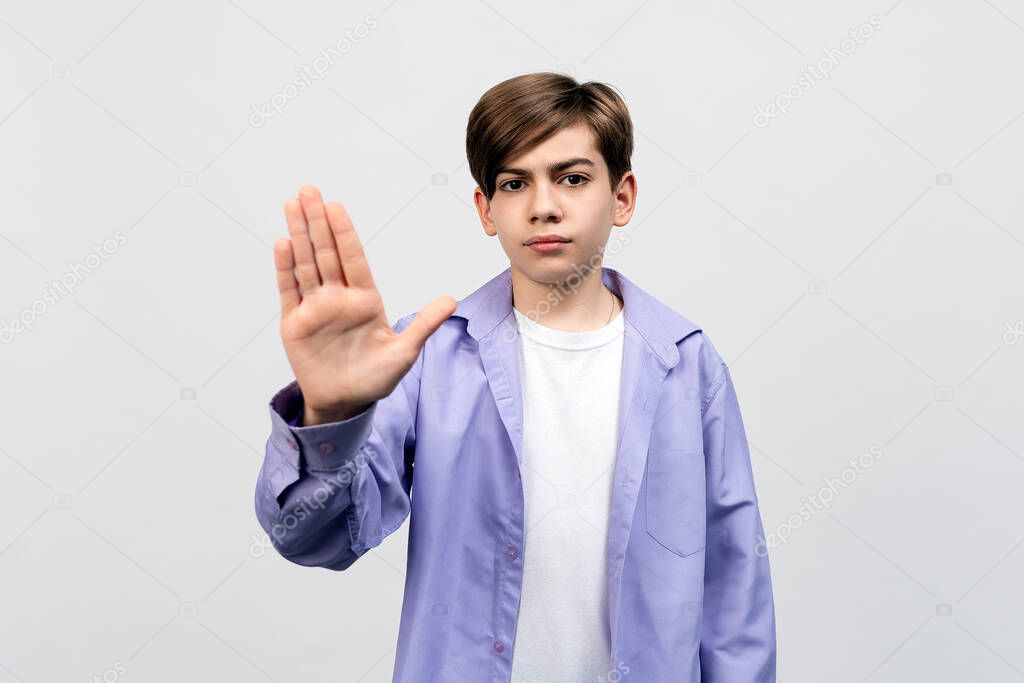 No. Serious boy shows stop prohibit gesture, keep your distance, stay away back off sign, standing displeased against light gray background