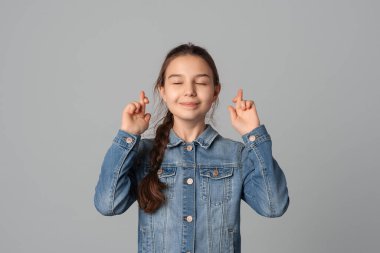 Güzel genç kız parmaklarını çapraz yaptı, arzulanan dilekler diledi, iyi haberleri bekledi, gri arka planda izole edilmiş, kot ceketli. Planların ve arzuların için tecrübe kavramı