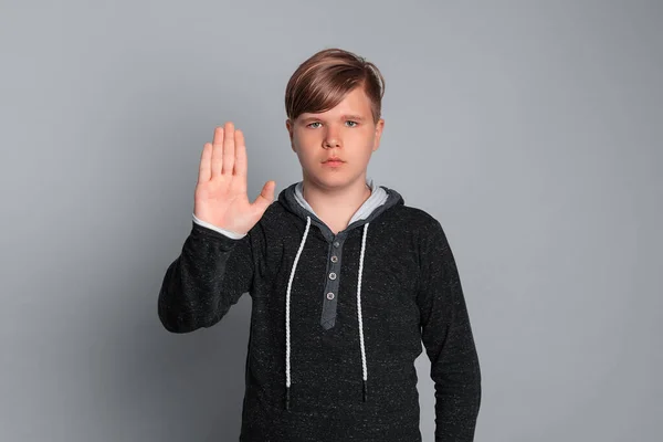 10代の少年は 負と深刻な顔の表情で手の手のひらで看板を停止し 灰色の背景に隔離され カジュアルな服を着ている 禁止の概念 — ストック写真