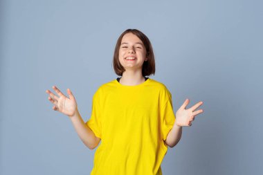 Açık gri arka planda duran sarı günlük tişörtlü mutlu genç kız portresi. Olumlu duygular kavramı