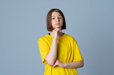 Sarı rahat tişörtlü güzel bir genç kızın portresi, kameraya çapraz kollu ve çenesi açık gri arka planda duran kendinden emin bir şekilde bakıyor. Düşünce kavramı
