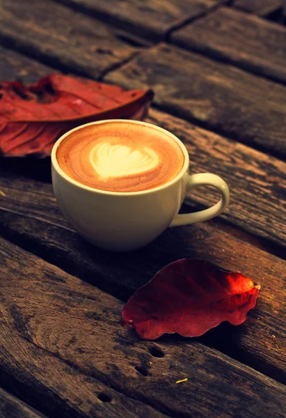 Taza de café con leche o capuchino sobre mesa de madera y hojas rojas — Foto de Stock