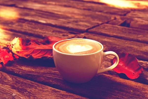 Taza de café con leche o capuchino sobre mesa de madera y hojas rojas — Foto de Stock