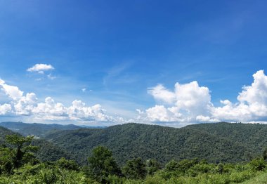 Arka planda mavi gökyüzü ve beyaz bulutları olan bir dağ. Doğa havası