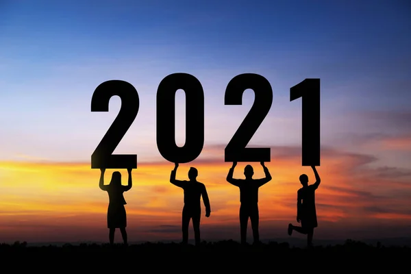 Silhouette people holding numbers 2021 with colorful dramatic sky at sunset. Concept for success in the future goal and passing time