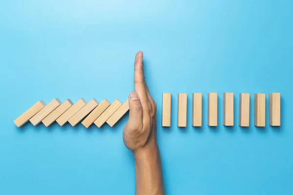 Ahşap masa mavisi üzerindeki domino etkisini durduran el. İş Riski Yönetimi Konsepti. İş stratejisi