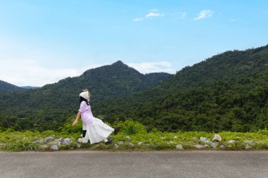 Nakhon Nayok, Tayland 'da Khundan prakanchon barajında oturan Asyalı bir kadın mutlu bir şekilde kolunu kaldırıyor. Dağ ve orman manzarası