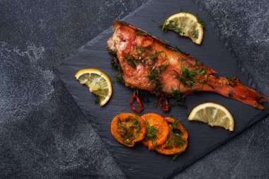 Fırınlanmış deniz levreği, domates biberli limon ve siyah tahta üzerinde siyah çimento arka planda duran otlar. Fırında pişmiş levrek balığı. Üst görünümü kopyala.