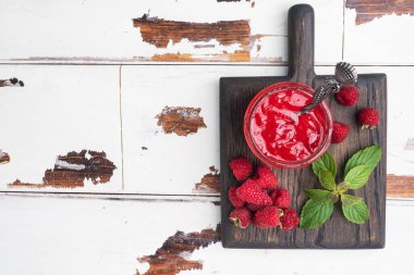 Cam kavanozda ev yapımı ahududu reçeli ve ahududu ve ahşap arka planda naneli taze ahududu kopyalama alanı.