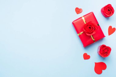 Sevgililer Günü kompozisyonu, mavi arka planda konfeti kalpleri ve güllerle dolu hediye kutusu. Düz yatıyordu