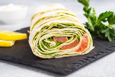 İnce pide ekmeği ruloları ve salata yapraklı kırmızı tuzlu somon gri beton arka planda duruyor. Boşluğu kopyala