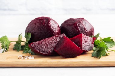 Haşlanmış pancarlar ve beyaz arka planda maydanoz yapraklarıyla kesilmiş bir tahta. Boşluğu kopyala,