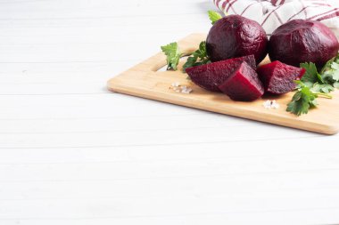 Haşlanmış pancarlar ve beyaz arka planda maydanoz yapraklarıyla kesilmiş bir tahta. Boşluğu kopyala,