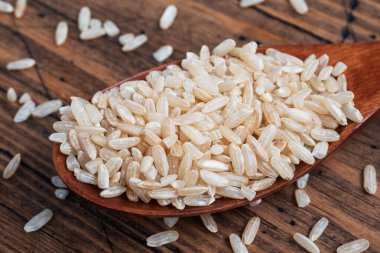 Kahverengi pirinç bir kaşık içinde çiğ uzun tahıl, ahşap arka plan örtüsü.