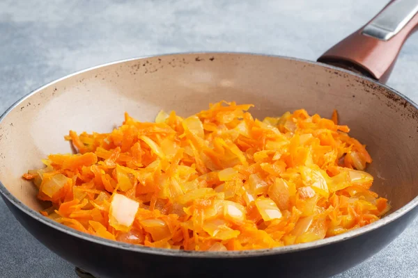 Fry grated carrots and chopped onions with oil in a frying pan gray concrete background.