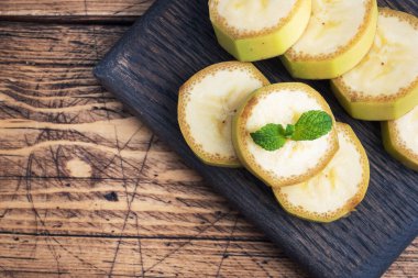 Muz ve dilimlenmiş muz, ahşap arka planda nane arkaplan görüntüsüyle, boşluğu kopyala