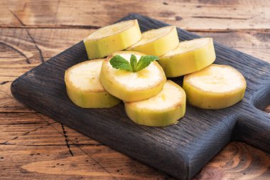 Muz ve dilimlenmiş muz, ahşap kırsal arka planda naneli.