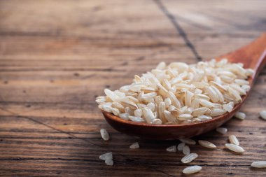 Kahverengi pirinç bir kaşık içinde çiğ uzun tahıl, ahşap arka plan kopyalama alanı