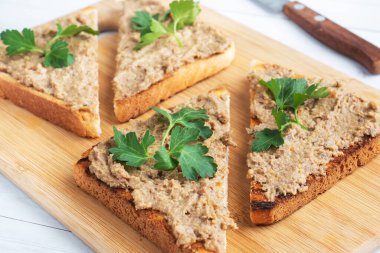 Tahta kesme tahtasının üzerinde maydanozlu sandviç ve ciğer ezmesi.