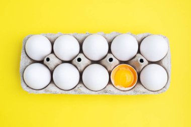 Pakette taze tavuk yumurtası, kutuda çiğ yumurta. Üst görünüm kopyalama alanı, sarı arkaplan. Kırık yumurta sarısı