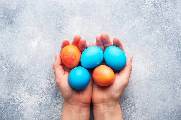 Easter eggs painted by hand colored on a concrete table, topview. copy space. In a woman\'s hands