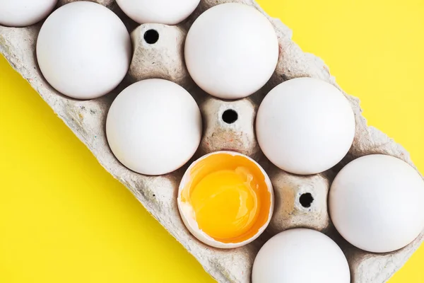 Fresh chicken eggs in a package, raw eggs in a white shell in a box. Top view copy space, Yellow background. Broken egg with yolk