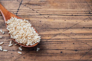 Kahverengi pirinç bir kaşık içinde çiğ uzun tahıl, ahşap arka plan kopyalama alanı