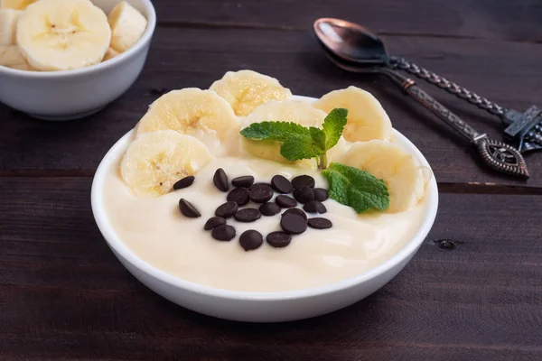 健康的な朝食 牛乳ヨーグルトバナナとプレート上のチョコレートとデザート 暗い木の背景 — ストック写真